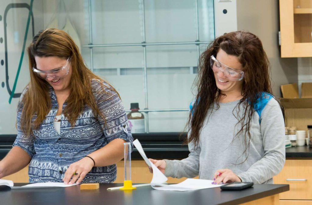 两个女学生微笑着一起做化学作业.